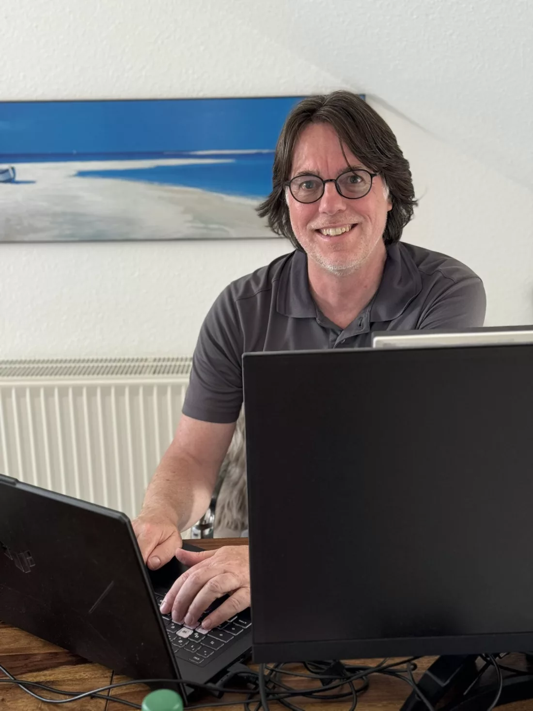 Oliver Werner arbeitet an seinem Schreibtisch mit KI-Werkzeugen an zwei Bildschirmen